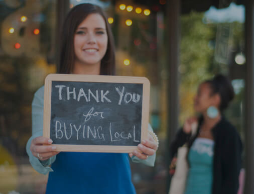 A woman holding up a signing saying Thank you for Buying Local.